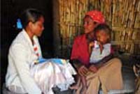 A health professional talks to a mother at her home. Her small child sits on her lap.