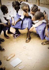 A group of girls seated on a bench looking at objects that lie on the ground.
