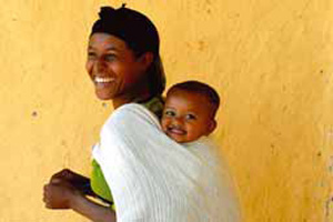 A smiling mother carries her laughing baby on her back.