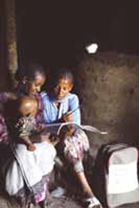 A health professional visits a mother at home. She shows her illustrated leaflets. A baby sits on the mothers knee.