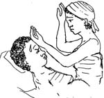 A woman is lying in a bed with sweat dripping off her forehead. A health professional is seated on the bed beside her. She has the back of one hand placed on the woman's head and the back of the other hand on her own head.