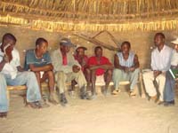 A group of men from the community are seated on a bench in a hut.