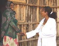 A health worker greets a woman who is standing at the entrance to her home.