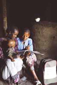 A health worker visits a mother at home. She shows her illustrated leaflets. A baby sits on the mothers knee.